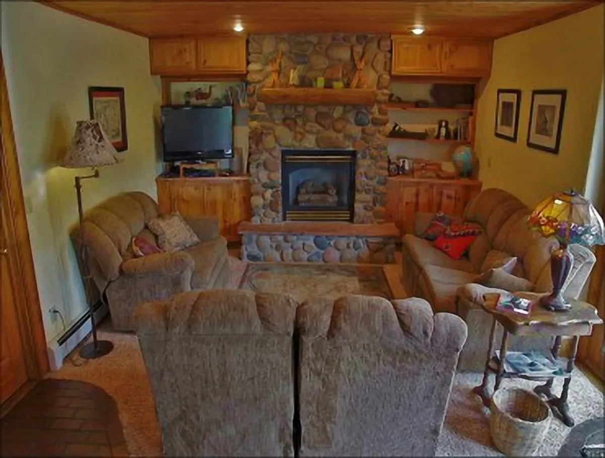 A welcoming living room centered around a fireplace, flanked by a comfortable sofa arrangement and wooden shelves. The space exudes warmth and is set up for relaxation, gathering, and sharing moments with friends or family. The scene is inviting, with soft lighting from a nearby lamp enhancing the cozy ambiance.